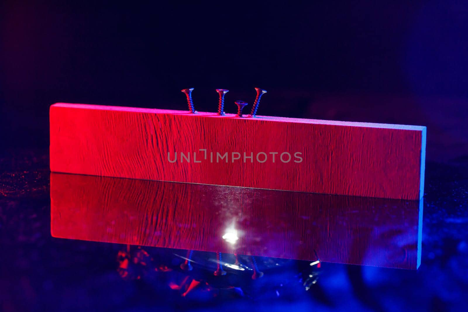 Screws screwed into a wooden beam in hard red light