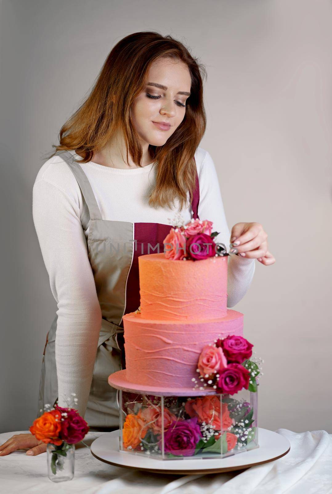 Beautiful girl confectioner in a working apron decorates a birthday cake with fresh flowers by aprilphoto