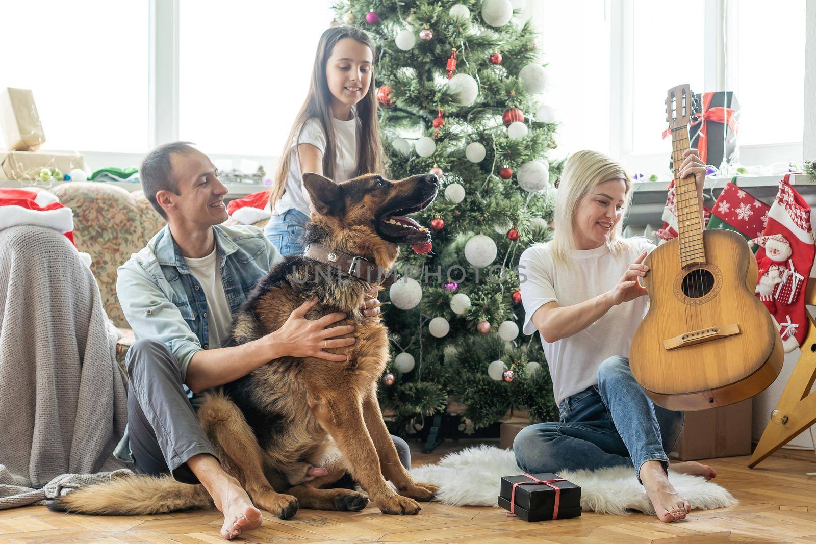 Merry Christmas and Happy New Year. Happy family with dog are waiting for the New Yearwhile sitting near beautiful Christmas tree at home