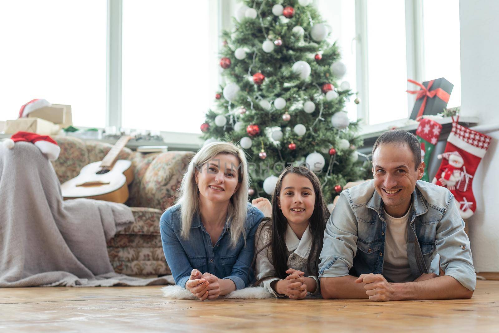 Merry Christmas and Happy New Year. Happy family on the living room floor one after another and laughing near beautiful Christmas tree at home. Happy family and kid.