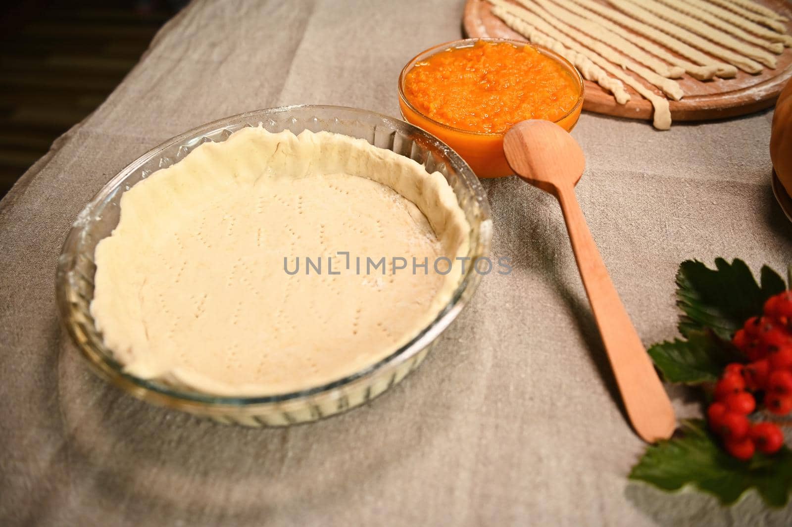 Close-up. Rolled out pastry dough in a baking dish, a bowl with pumpkin puree, a branch with viburnum berries on a table with linen tablecloth. Still life with ingredients for making Thanksgiving pie