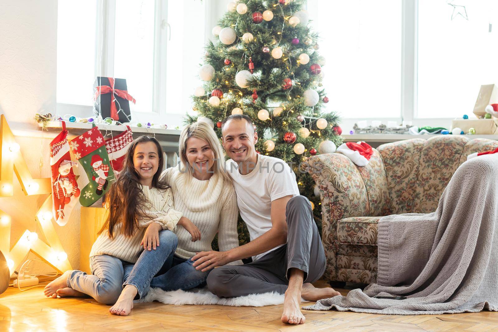 Christmas Family. Happiness. Portrait of dad, mom and daughter sitting at home near the Christmas tree.