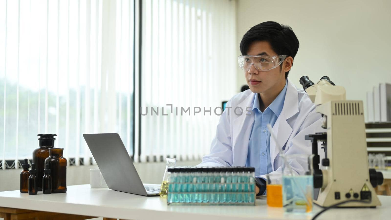 Young asian male research scientists in white coat using laptop computer at laboratory.