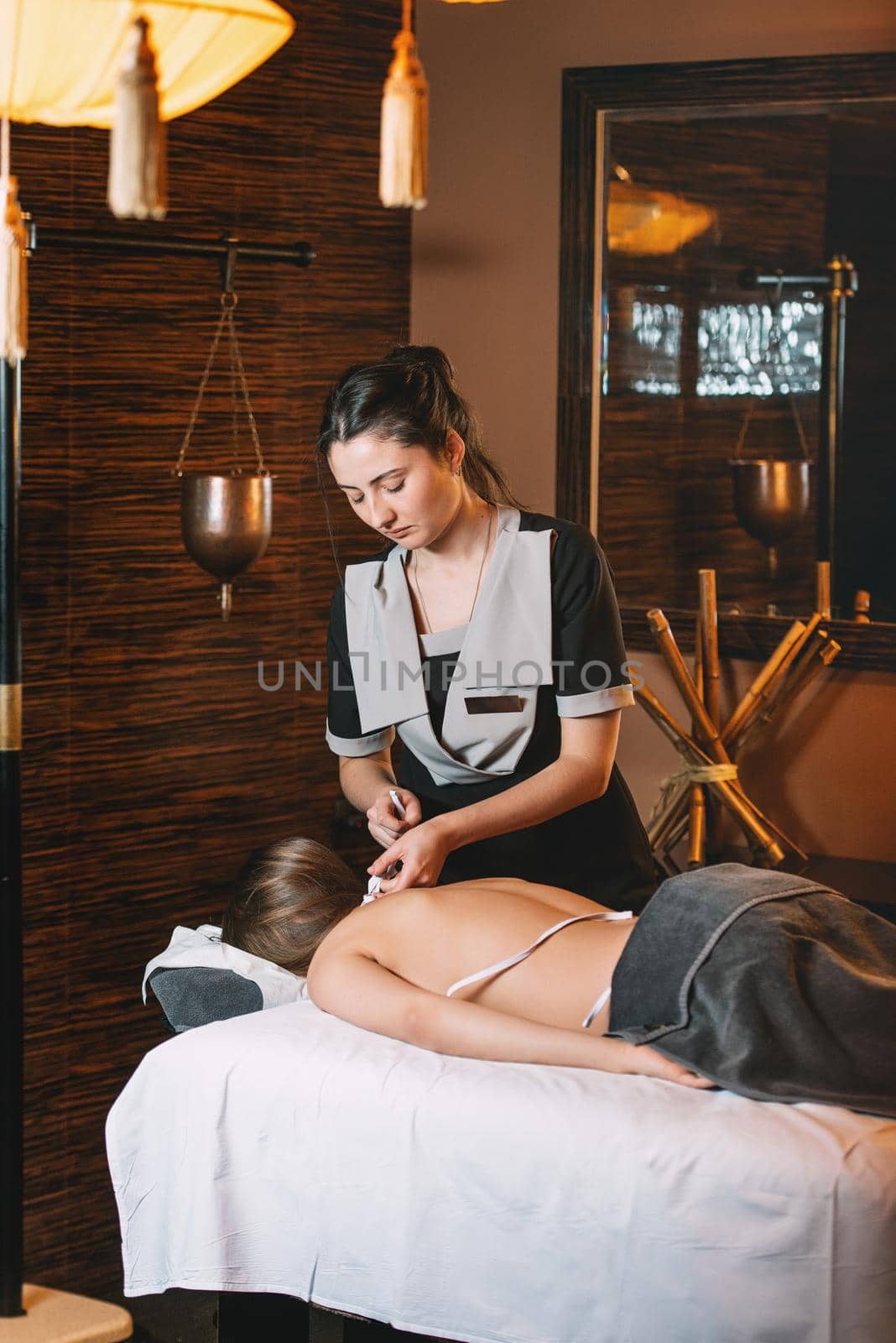 Young charming girl on a panchakarma procedure laying on a massage table. beautiful woman spending time at modern spa cabinet relaxing. Soft yellow light.