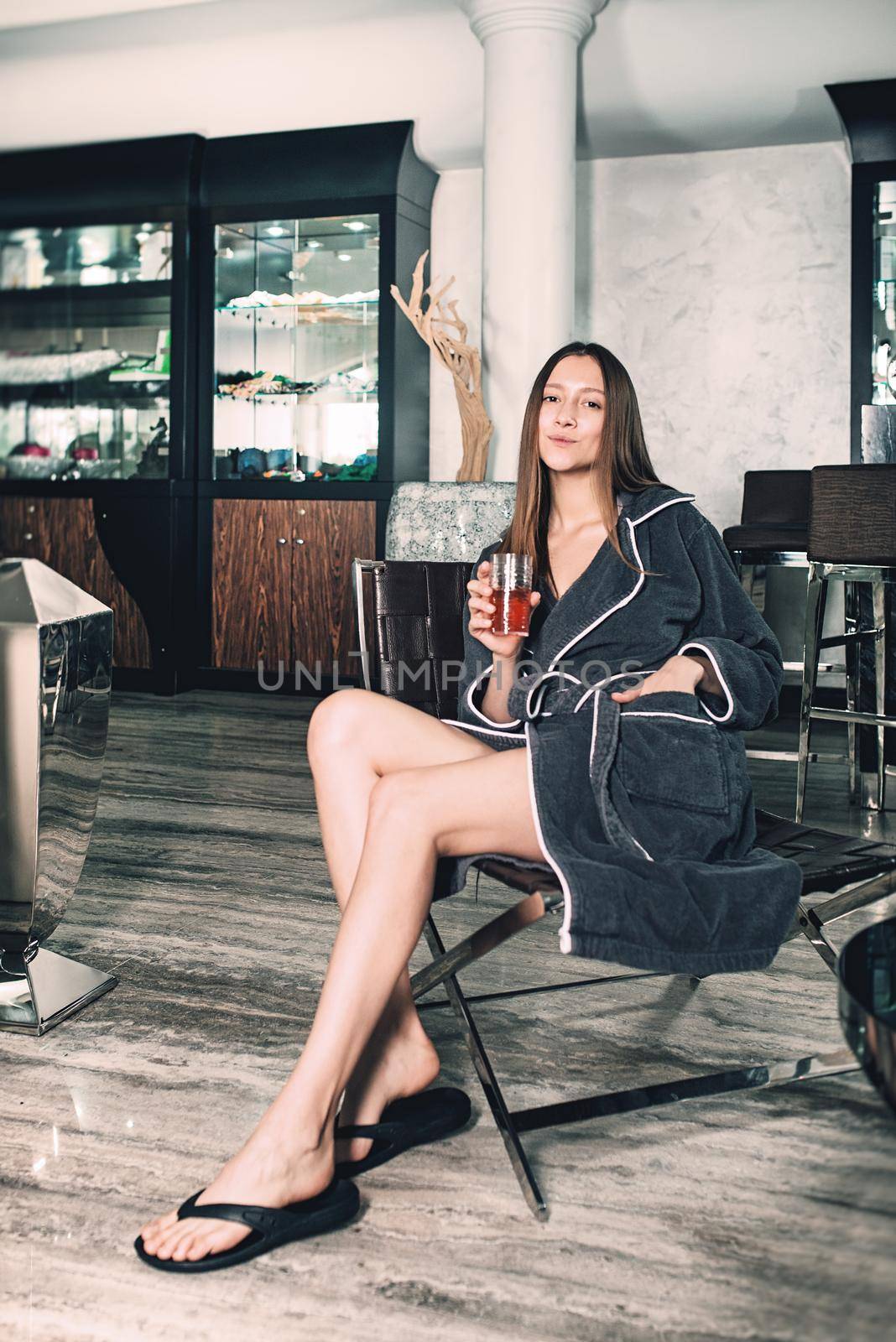 Portrait of young beautiful woman relaxing in a chair in a bathrobe with a detox drink in a hand. Luxery spa center