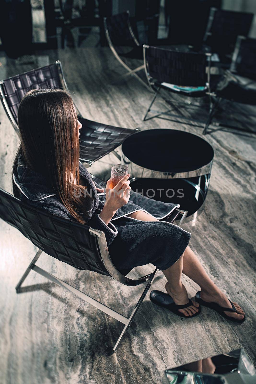 Portrait of young beautiful woman relaxing in a chair in a bathrobe with a detox drink in a hand. Luxery spa center