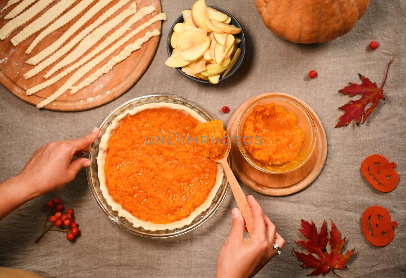 Top view of a woman filling rolled dough in baking dish with mashed pumpkin, making homemade pie for Thanksgiving dinner by artgf