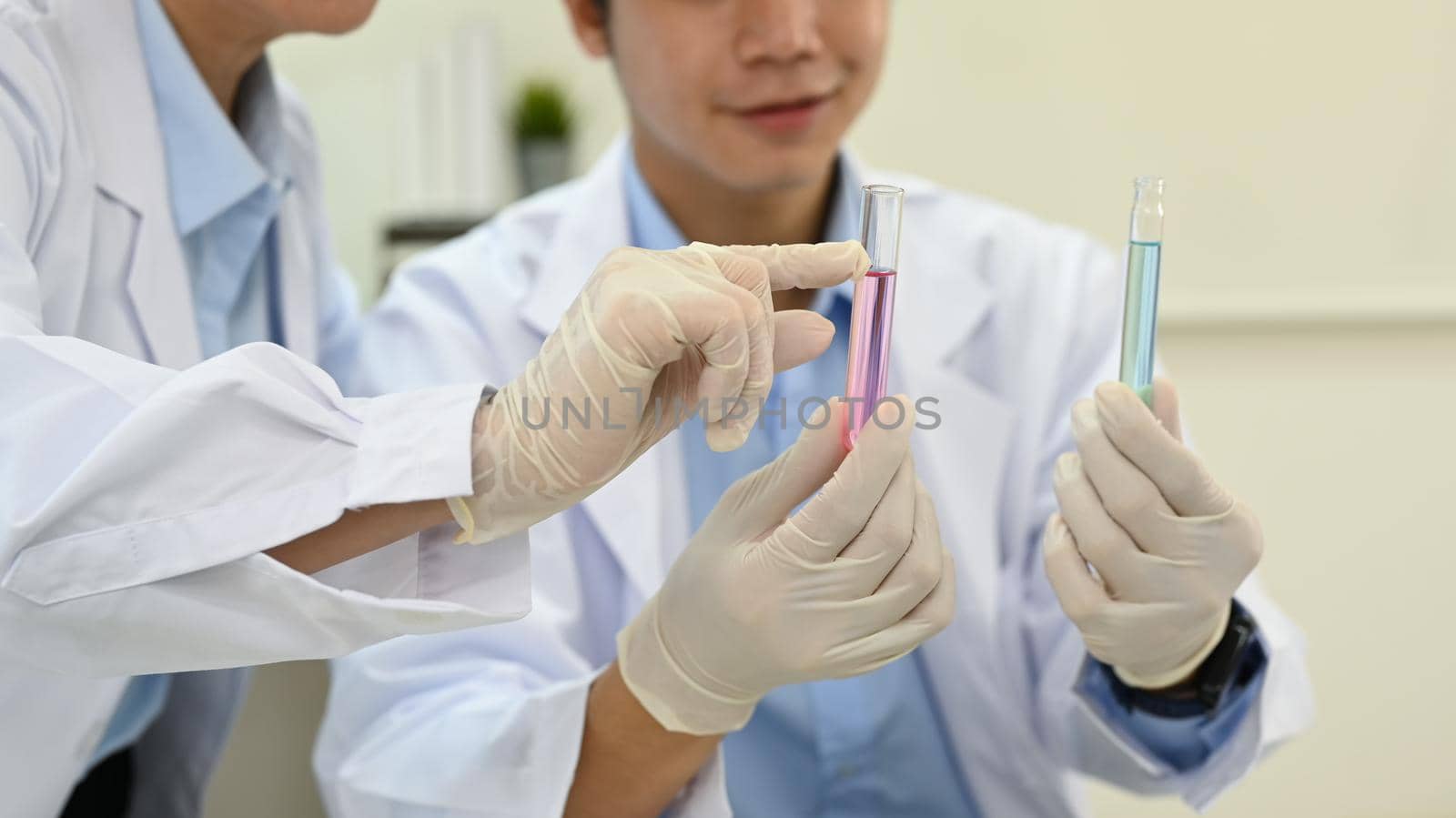 Cropped shot of senior supervisor and young man specialist analyzing liquid biochemicals, conducting experiment in laboratory by prathanchorruangsak