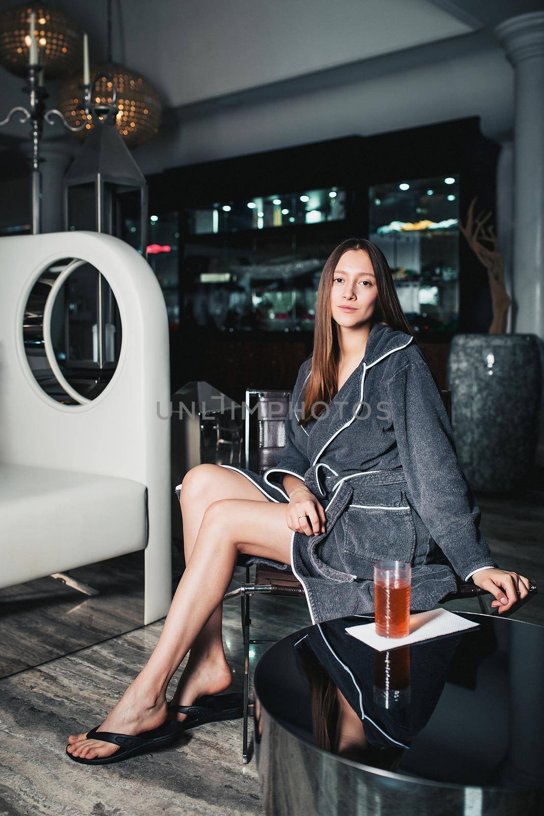 Portrait of young beautiful woman relaxing in a chair in a bathrobe in spa center
