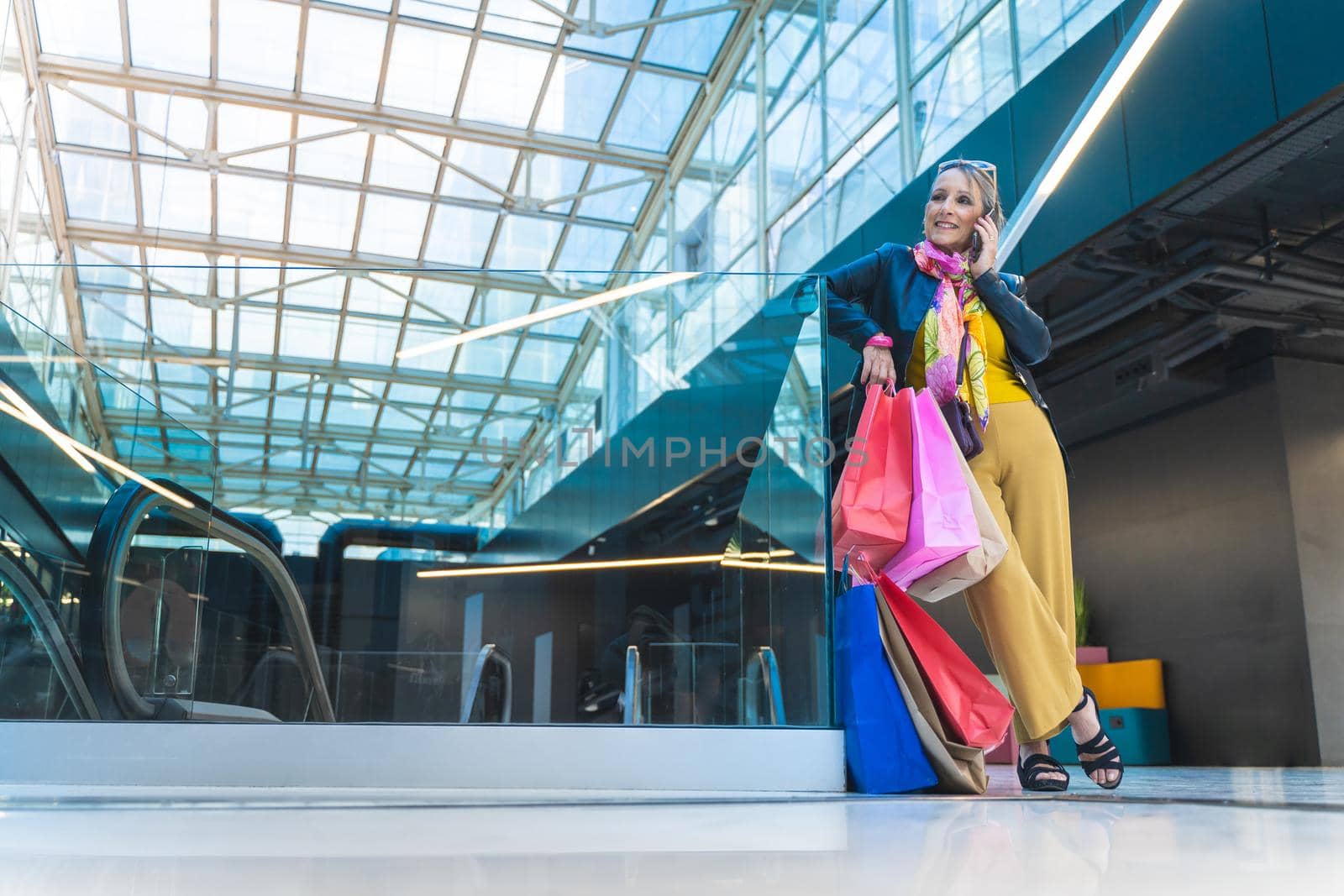 Mature woman talking smartphone with shopping bags in the mall. High quality photo