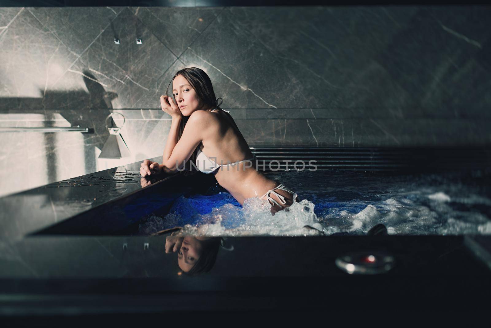 Sexy beautiful caucasian woman relaxing in a pool with jacuzzi. Dark room. Poor lighting.