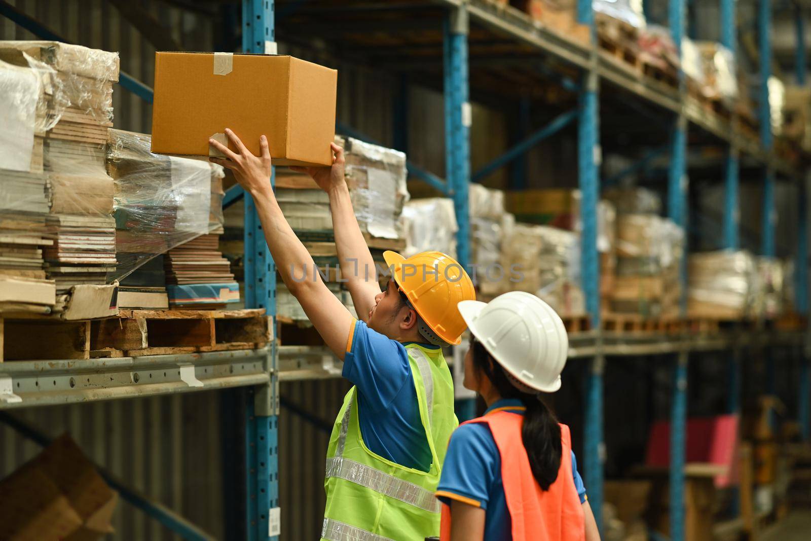 Image of warehouse workers checking inventory and quantity of storage product on shelf full of packed boxes and goods.