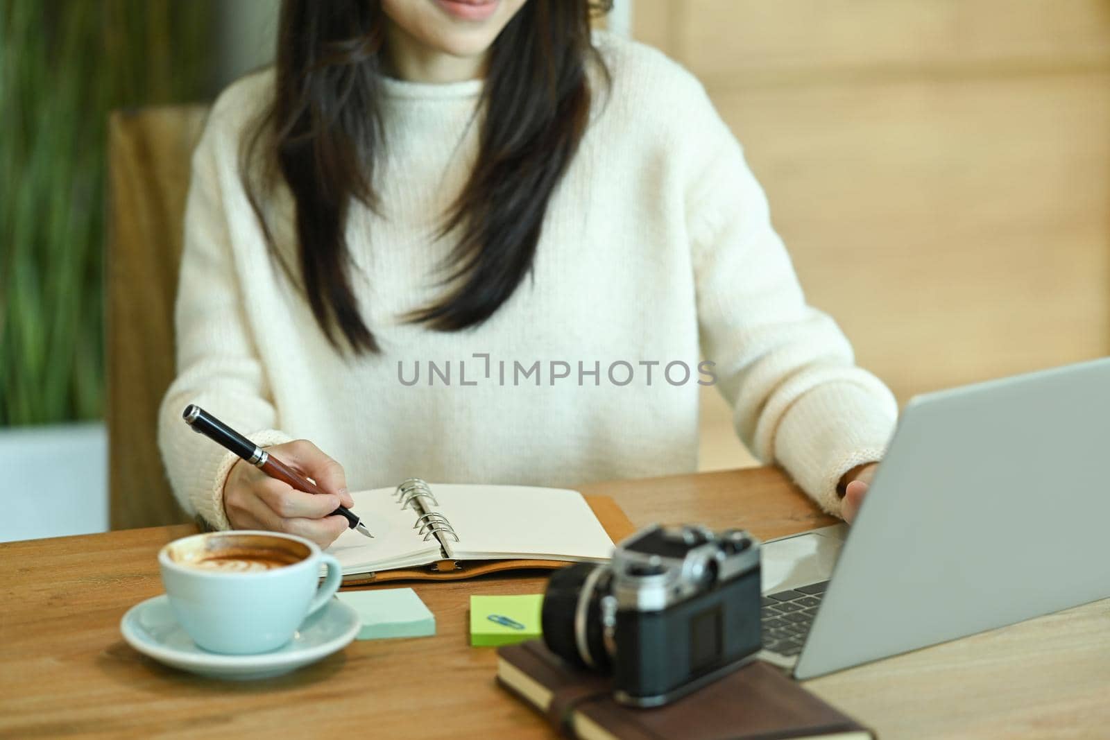 Young asian woman in white sweater holding pen and making notes to her diary.