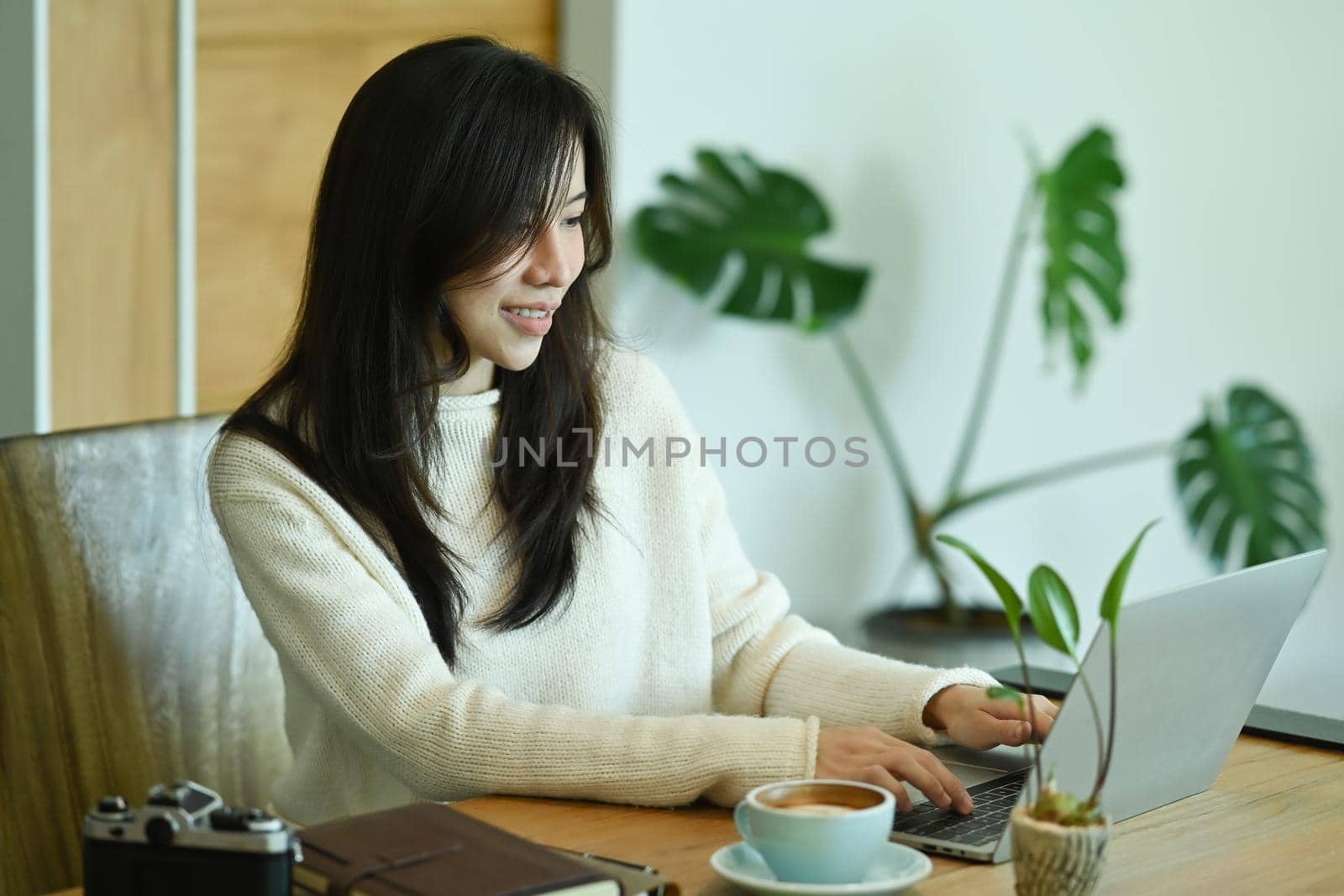 Thoughtful asian woman in white sweater using laptop computer at home.