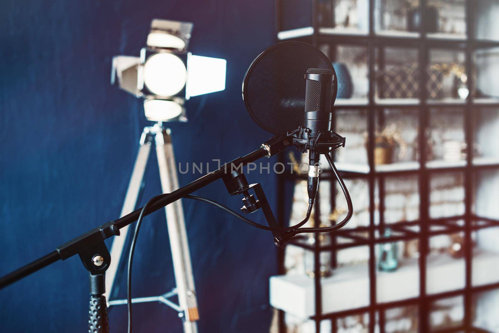 Close up studio condenser microphone with pop filter and anti-vibration mount live recording. Blue wall and decorative light on a background.