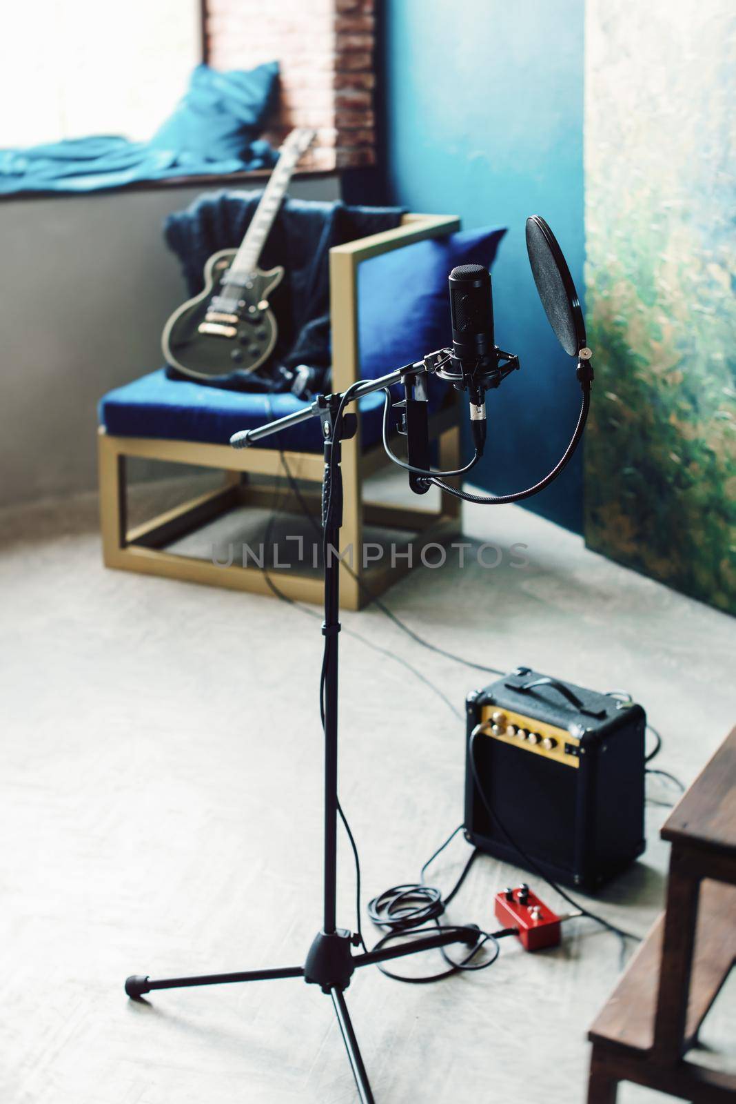 studio condenser microphone with pop filter and anti-vibration mount live recording. Blue wall, speaker and guitaron a background.