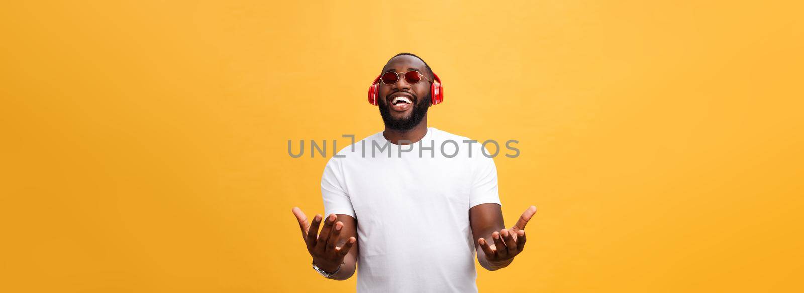 Handsome young African American man listening and smiling with music on his mobile device. Isolated over yellow background. by Benzoix