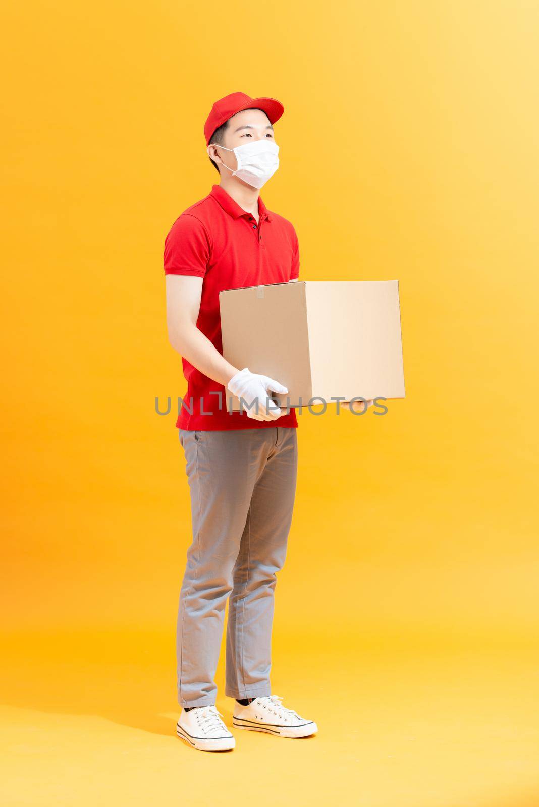 Courier in protective mask and medical gloves holding cardboard box to deliver