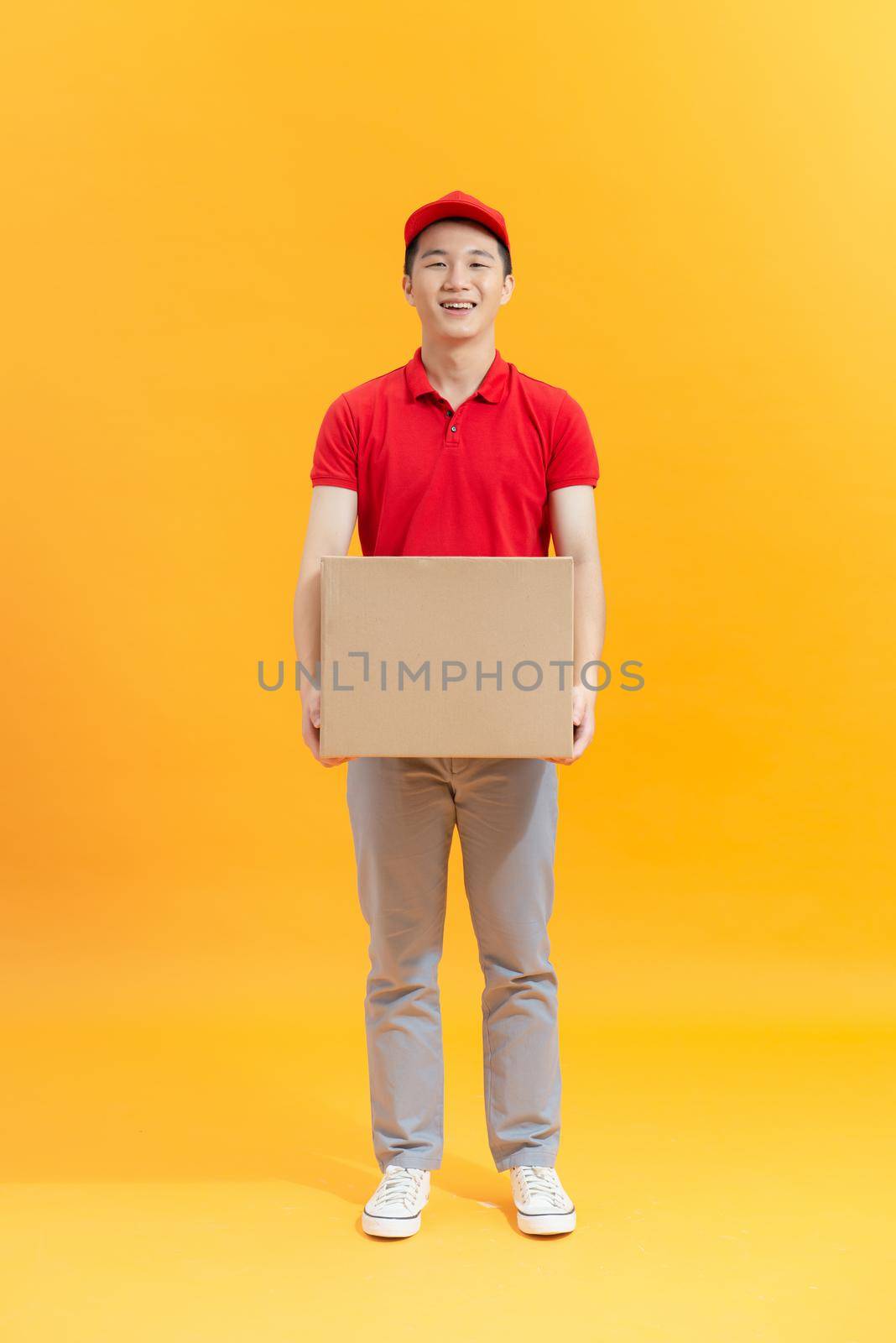 Cheerful delivery man. Happy young courier holding a cardboard box and smiling  by makidotvn