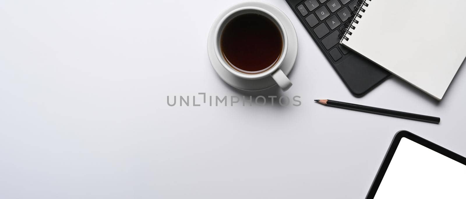 Cup of coffee, notebook and digital tablet on white table. Minimal workspace.