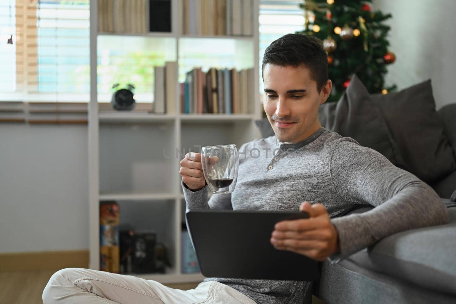 Young man in casual cloth drinking coffee and using digital tablet at home.