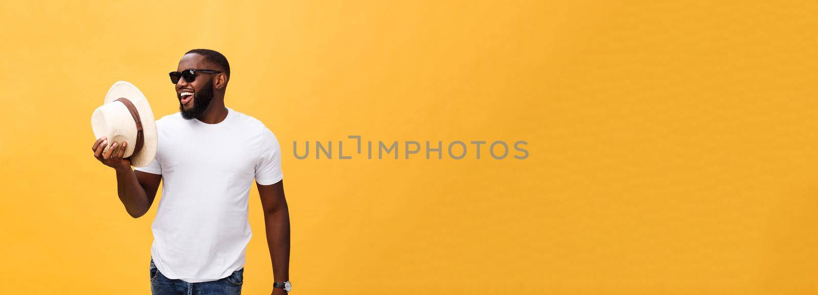 Close up portrait of a young man laughing with hands holding hat isolate over yellow background.