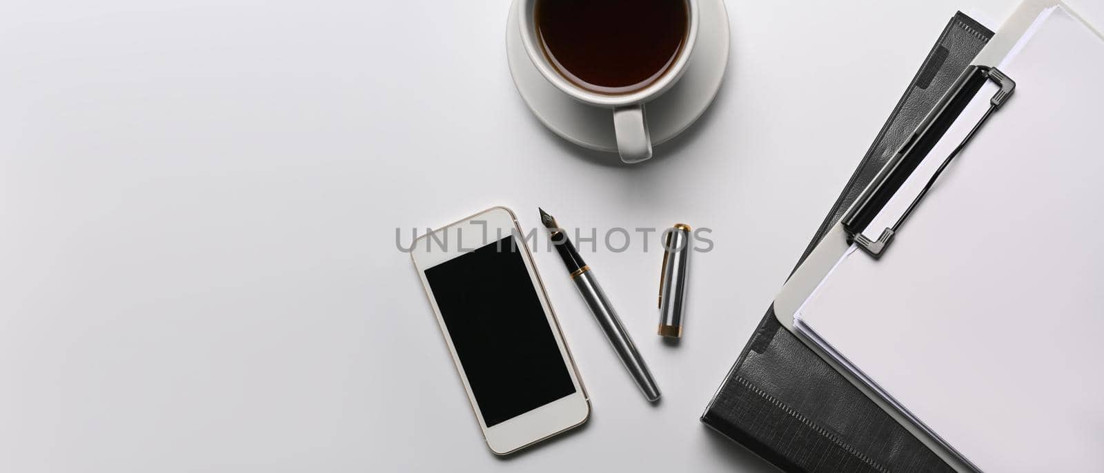 Mock up mobile phone, coffee cup and clipboard on white office desk.