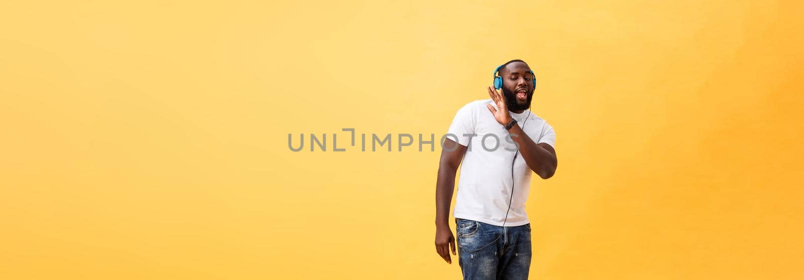 Full length portrait of a cherry young african american man listening to music with headphones and dancing isolated over yellow background.