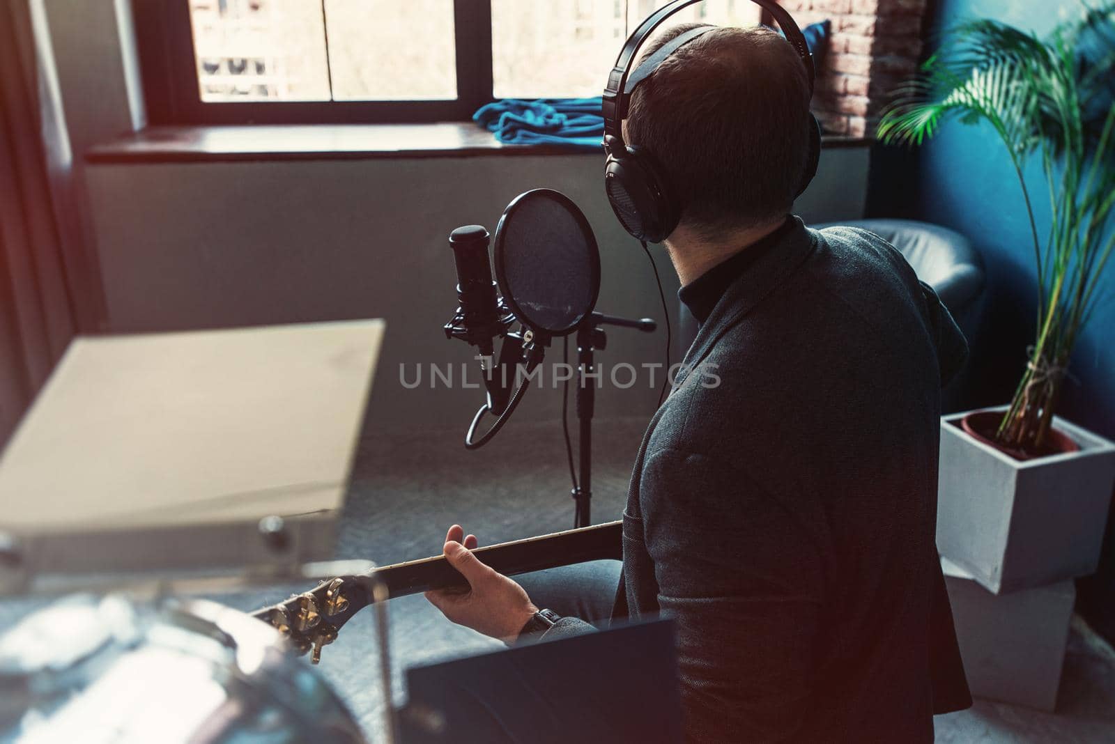 Close up of a man singer sitting on a stool in a headphones with a guitar recording a track in a home studio by Ashtray25