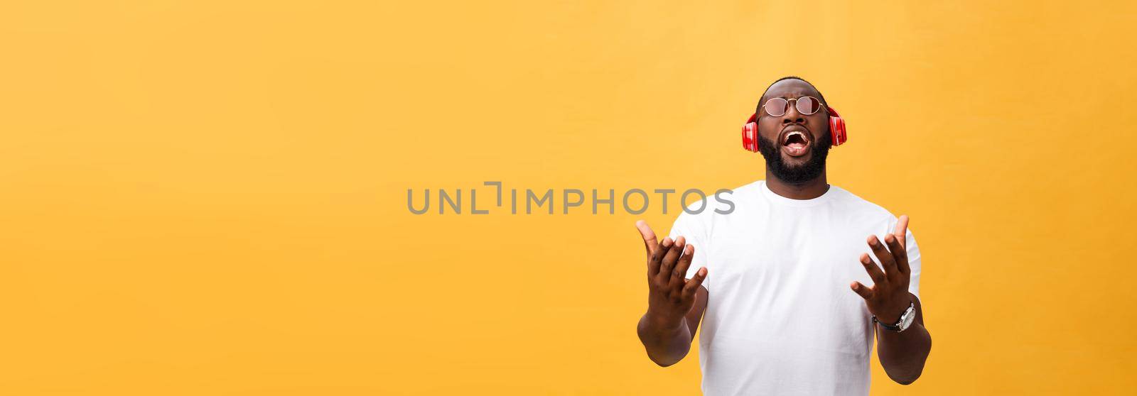 Young African American man wearing headphone and enjoy music over yellow gold Background.