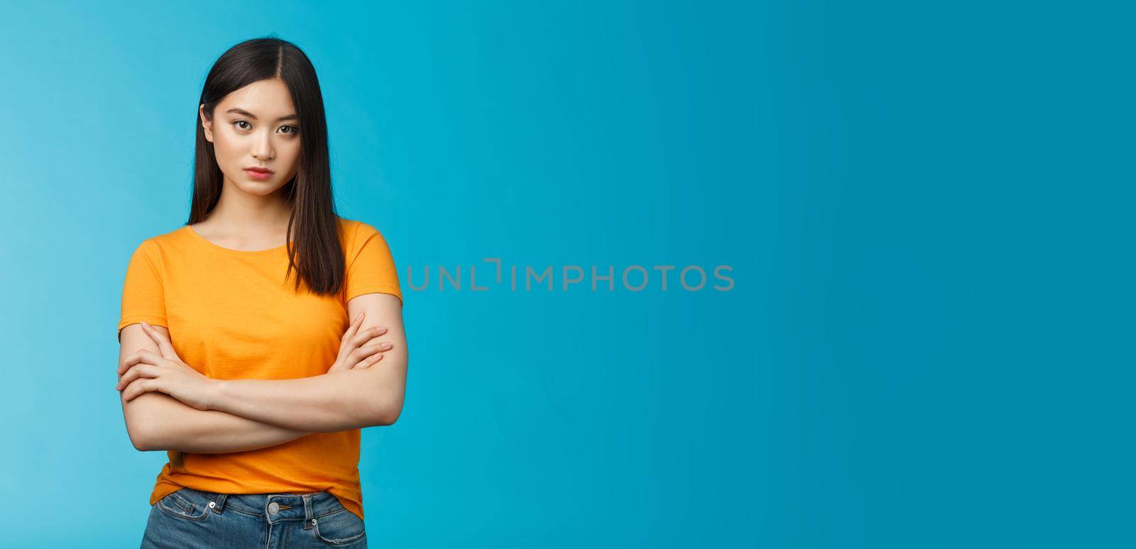 Serious-looking confident and arrogant asian woman cross hands chest powerful ignorant pose, look indifferent strict bored face, stand blue background unimpressed, demand answers. Copy space