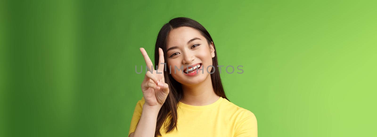 Close-up joyful cute asian girl lively look camera smile, show peace victory sign entertained, grinning posing photograph tender expression, stand green background positive and lucky.