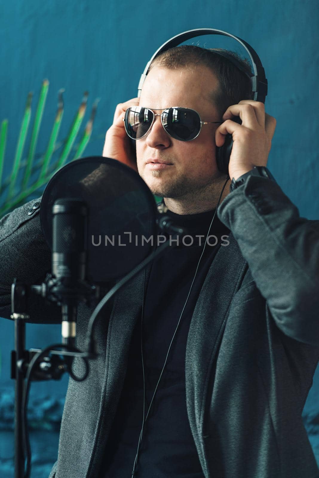 Close up of a man singer in a headphones recording a song in a home studio. Man wearing sunglasses, black shirt and a jacket. side view