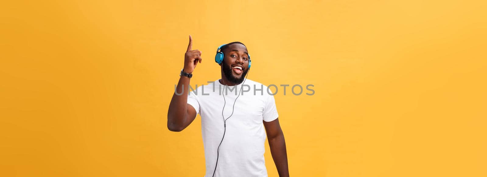 Young African American man wearing headphone and enjoy music dancing over yellow gold Background.