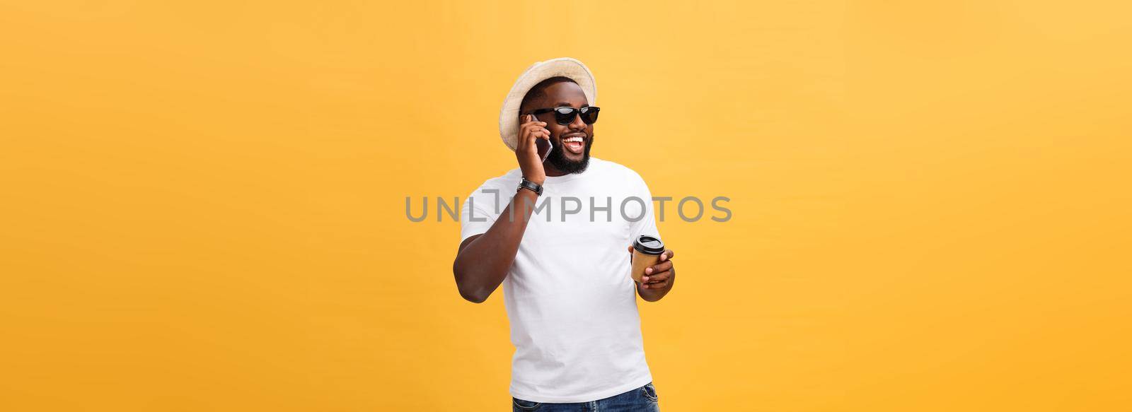 Handsome African American with mobile phone and take away coffee cup. Isolated over yellow gold background