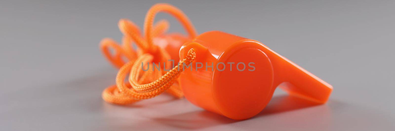 Close-up of orange sport whistle on grey surface, tool for school trainers. Side view of whistle, loud sound maker. Sport competition equipment concept