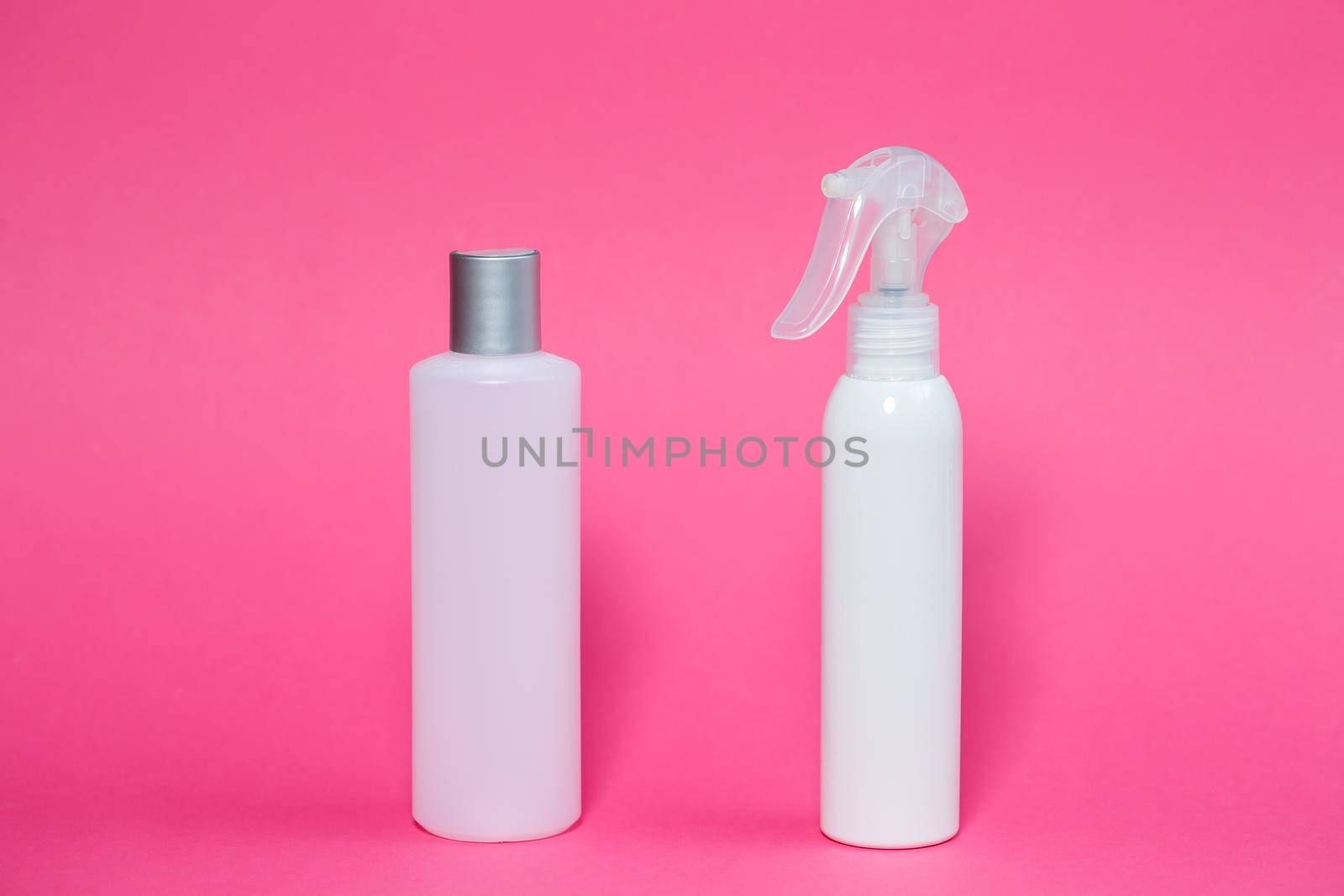 Two white bottles with shampoo for hair, body gel, spray for the skin on a pink background