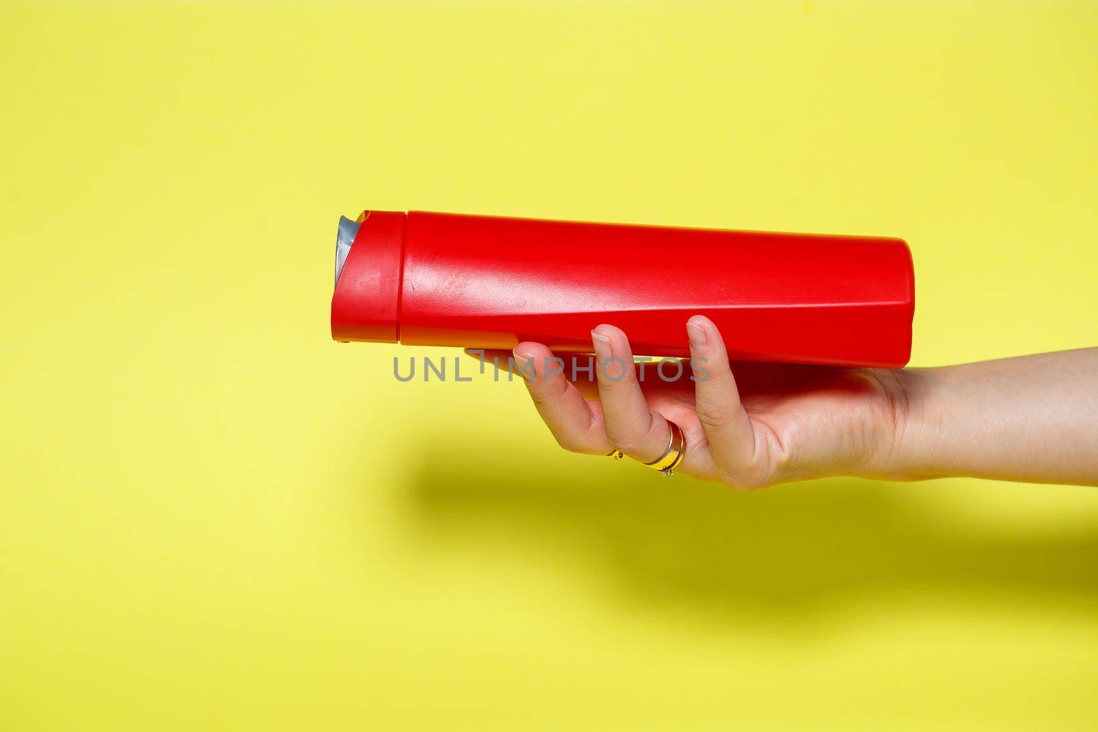 Red bottle in hands with gel shampoo or liquid soap on a yellow background
