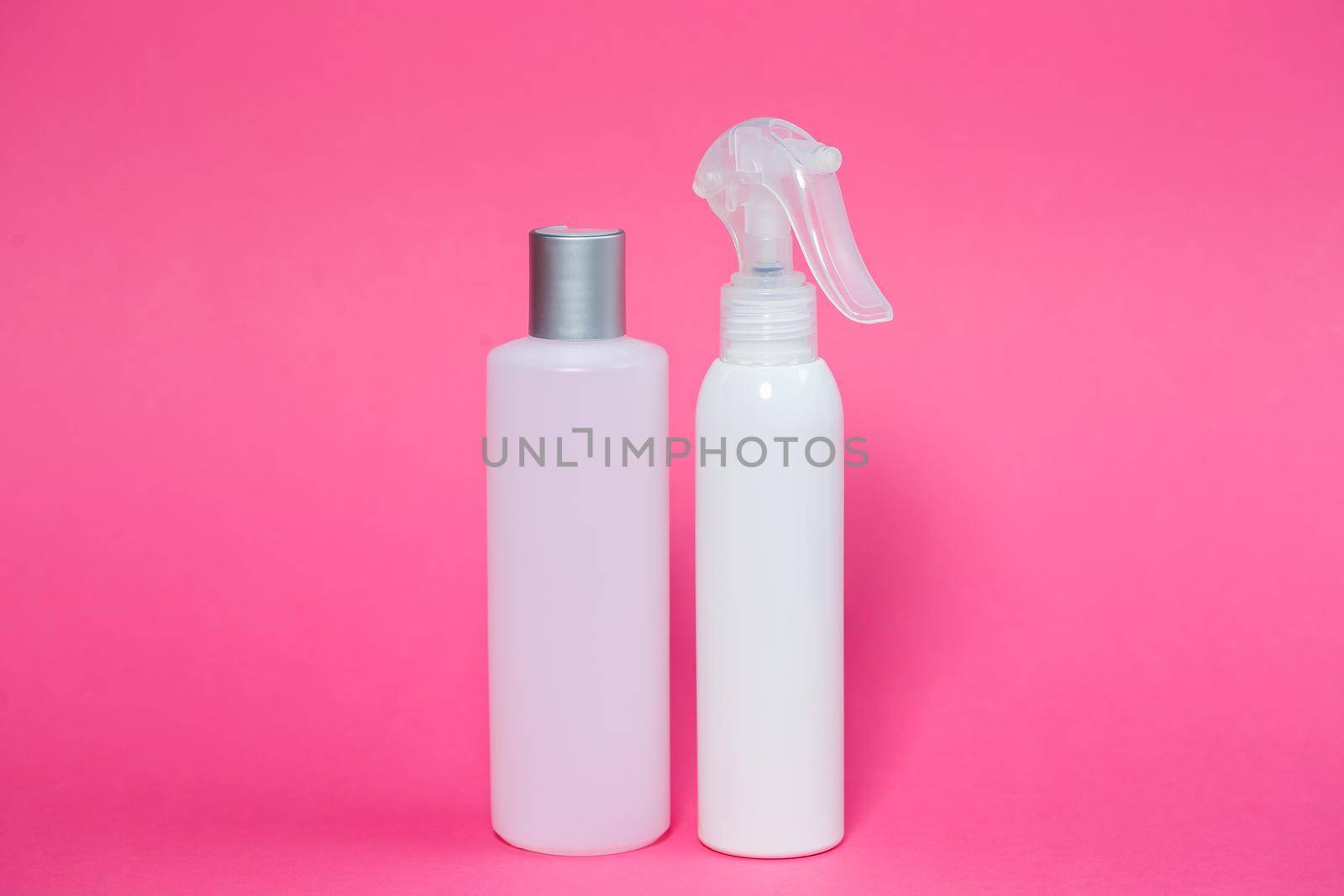 Two white bottles with shampoo for hair, body gel, spray for the skin on a pink background