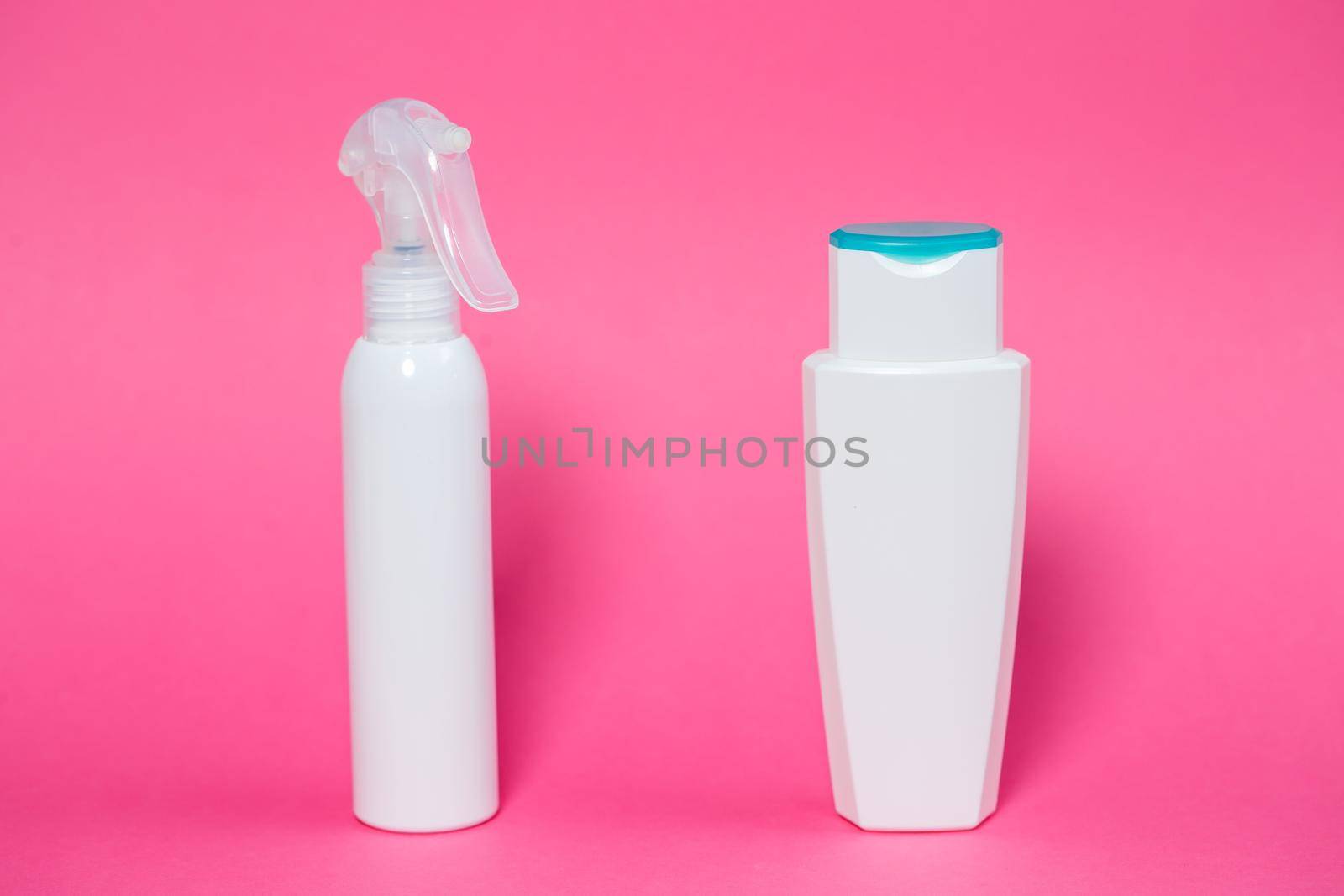 Two white bottles with shampoo for hair, body gel, spray for the skin on a pink background