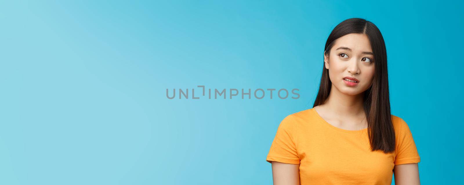 Doubtful unsure cute asian girl dark short haircut look left questioned, see strange thing, open mouth frowning upset uncertain, have hesitations, peek suspicious aside, stand blue background by Benzoix