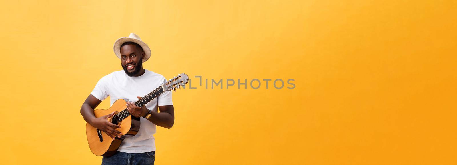 Muscular black man playing guitar, wearing jeans and white tank-top. Isolate over yellow background