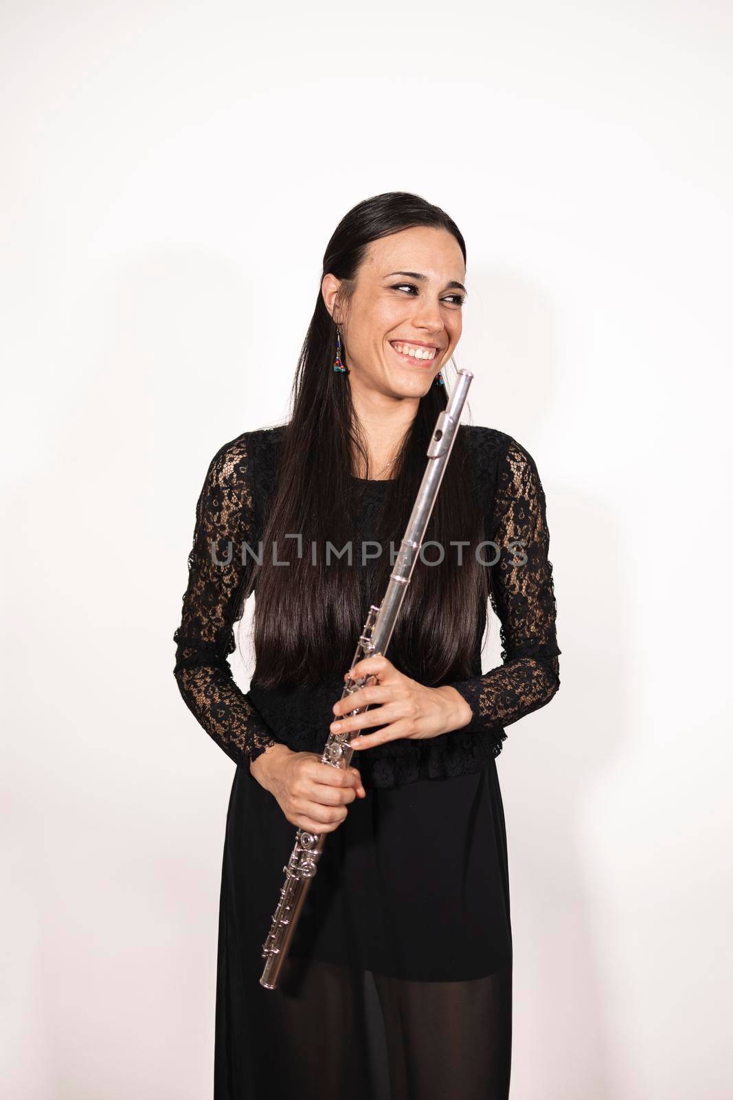 A young elegant female flutist smiling at camera while holding her instrument by stockrojoverdeyazul