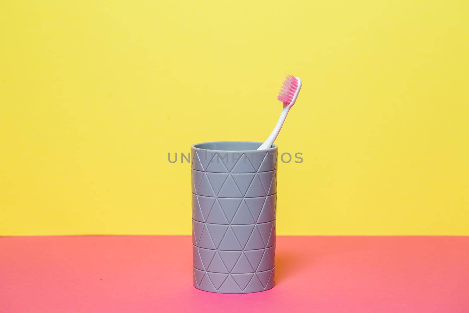 A pink toothbrush is standing in a gray glass. Dental care concept by Dmitrytph
