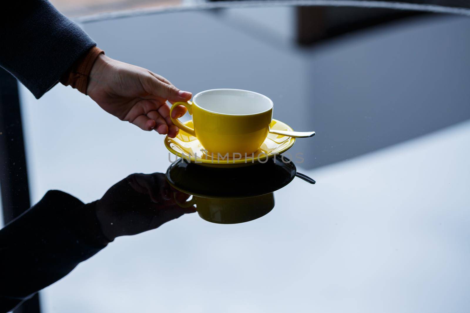Yellow cup for coffee or tea with a saucer in the hands of a girl on the background of a glass table.