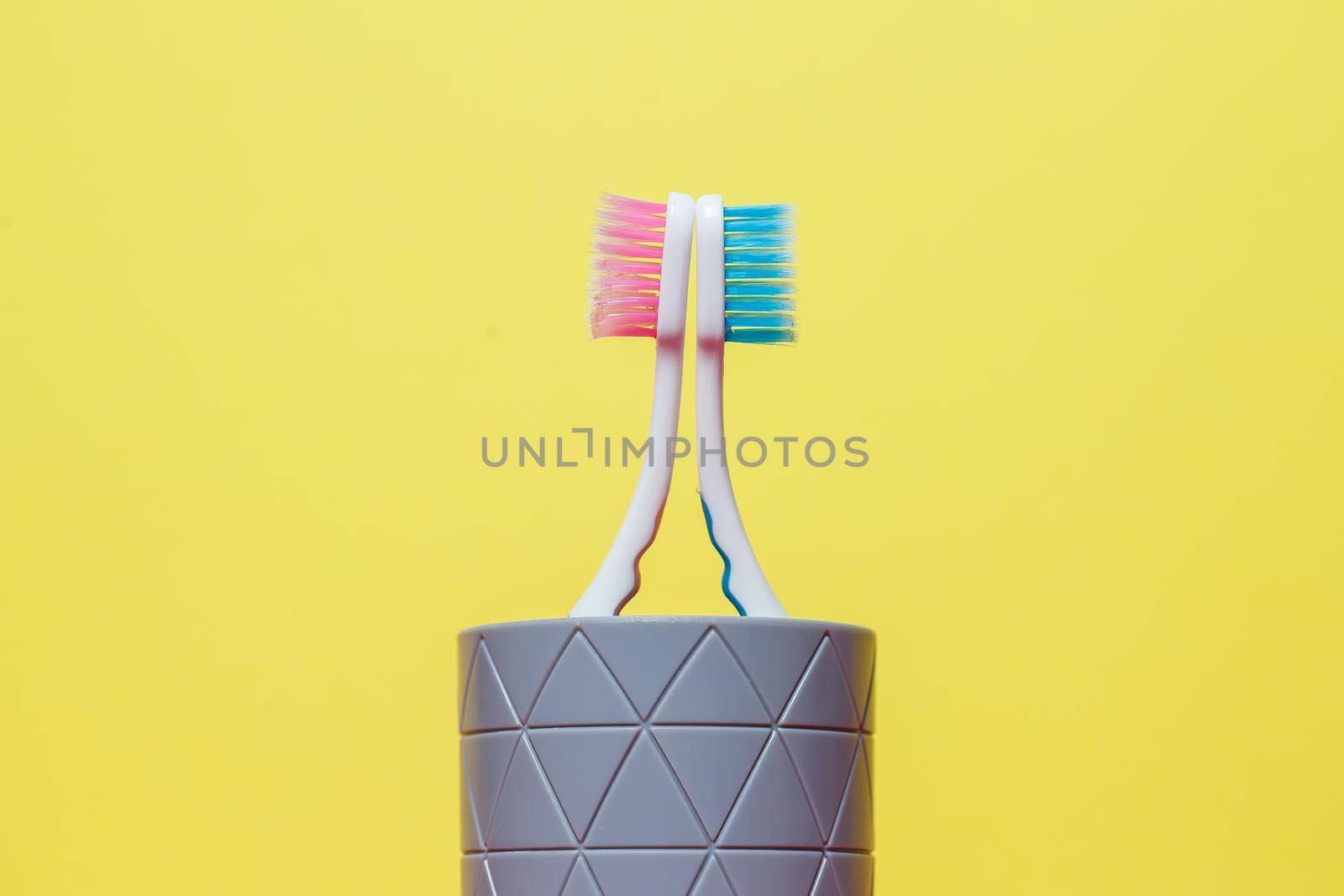 Two toothbrushes stand with a gray glass on a yellow background. Toothbrush concept for a couple, living together as the beginning of a family