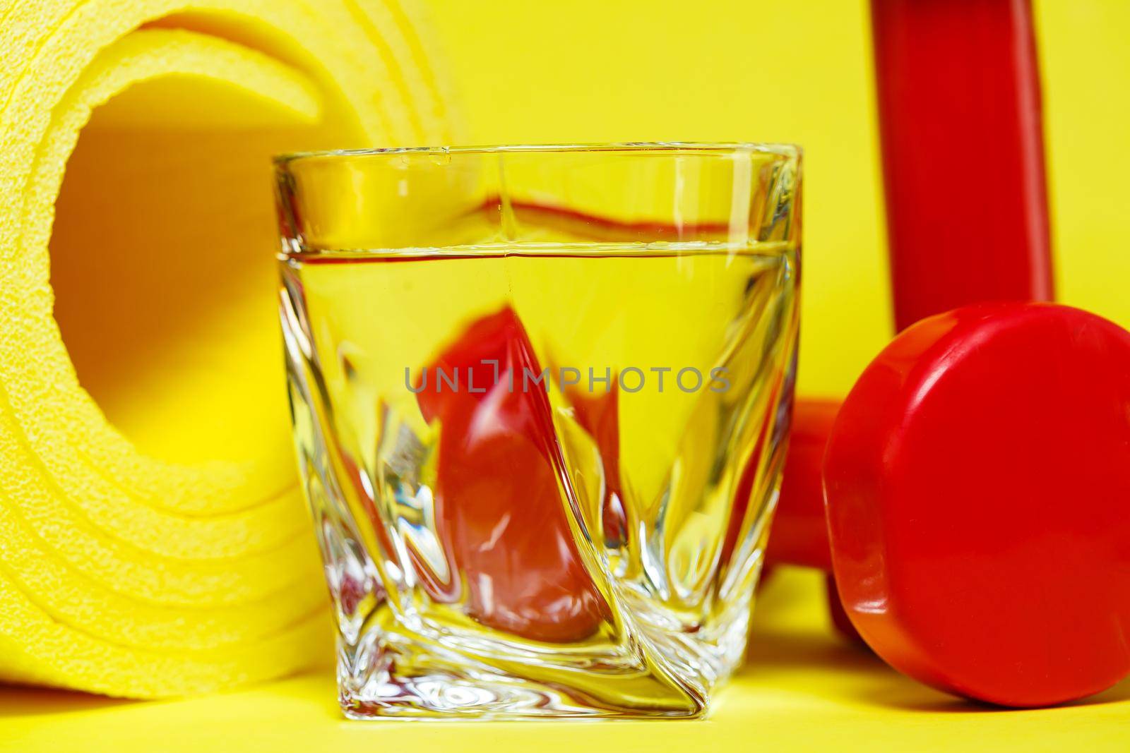 red dumbbells, a glass of water, a yellow rug, colored background, sports, energy drink, equipment for the gym