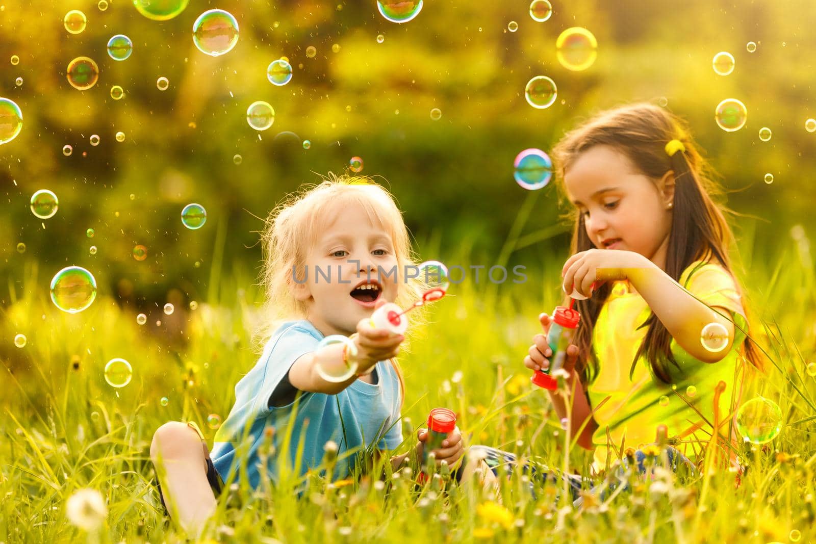 Two cheerful cute girls are playing outdoors with huge soap bubbles.