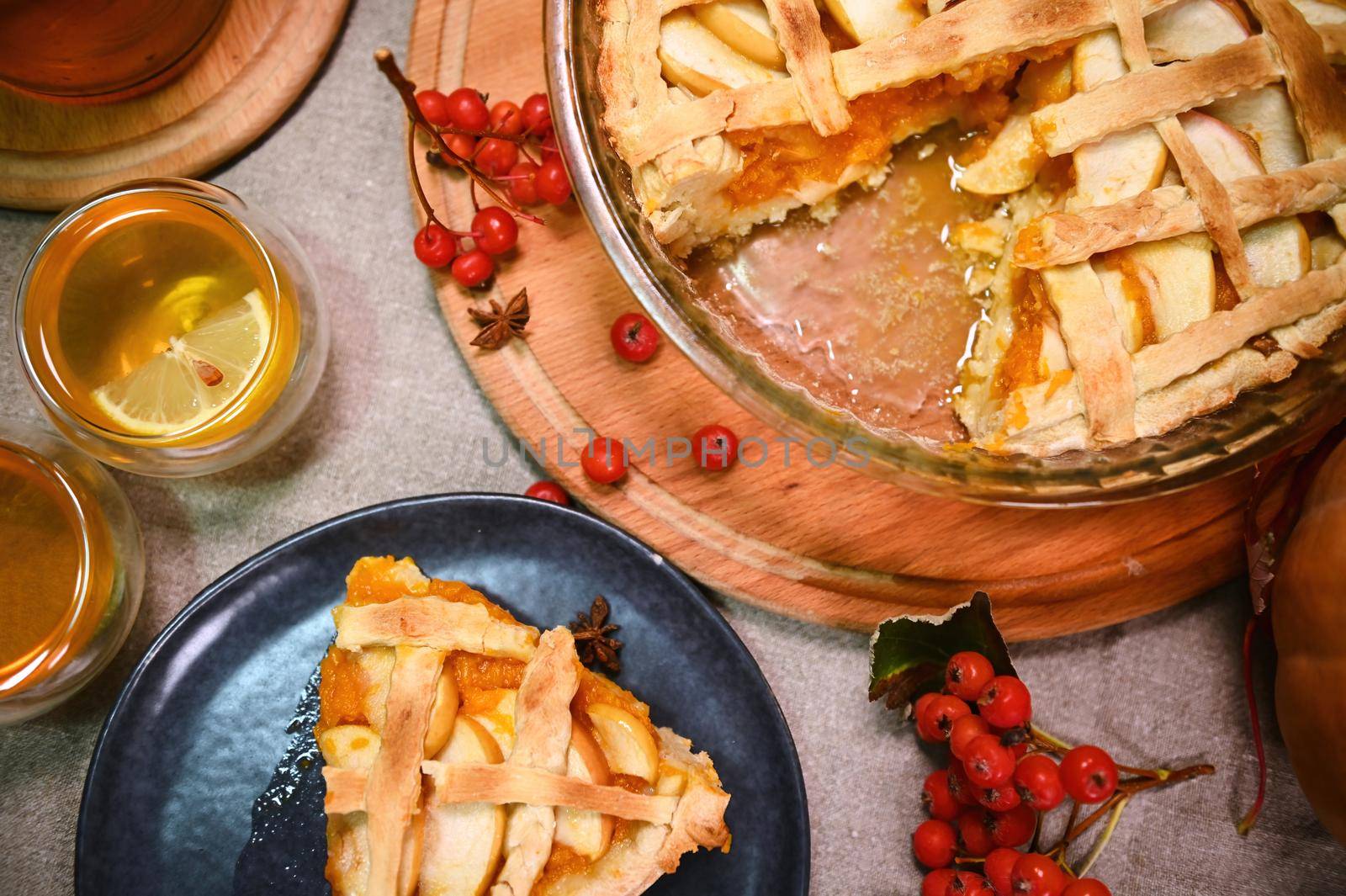 Cropped view. View from above of delicious homemade American classic pumpkin apple pie with crispy crust for Thanksgiving Day. Still life with food, healthy antioxidant herbal tea and viburnum berries