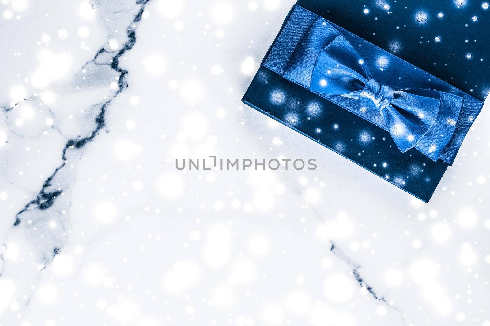 Branding, glamour and cold season concept - Winter holiday gift box with blue silk bow, snow glitter on marble background as Christmas and New Years presents for luxury beauty brand, flatlay design